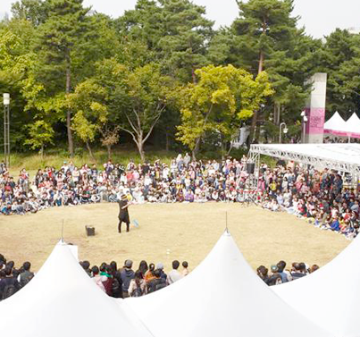 한글박물관 밖 잔디밭에 수많은 관람객들이 원을 두르고 앉아 마임 및 마술 공연을 관람하고 있다.