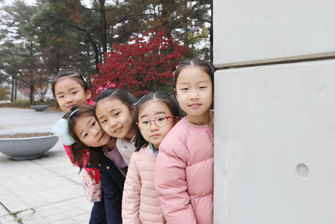 다섯 소녀가 기둥에 몸을 기대고 고개만 빼꼼 내민채 카메라를 바라보고 있다.