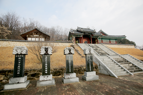 
상주 임란 북천 전적지를 계단 아래서 올려다본 모습. 커다란 기와 건물 돌담 아래로 돌계단과 네 개의 비석이 자리해 있다.