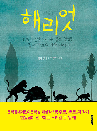 도서 《해리엇》의 표지. 표지 한가운데 제목 ‘해리엇’이 적혀있다. 그 아래 ‘175년 동안 바다를 품고 살았던 갈라파고스거북 이야기’가 적혀 있다. 뿌연 청록색 배경에 원숭이, 거북이 등 동물 네 마리의 그림자가 나란히 걸어가는 모습이 그려져 있다. 뒤로는 어두운색의 나무 네 그루가 듬성듬성 그려져 있다. 표지 하단에는 노란 배경 위에 ‘문학동네어린이문학상 대상작 『봉주르, 뚜르』의 작가 한윤섭이 선보이는 스케일 큰 동화!’가 적혀 있다. 