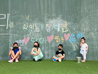 잔디밭에 세워진 벽 앞에 네 명의 아이들이 있다. 세 명의 아이들은 쭈그려 앉아있으며 한 명의 아이는 서있다. 각자 뒤에 있는 벽에 자신의 이름과 하트를 분필로 그려놓았다. 그 외 문구로 ‘화이팅! 정세연’ 등이 적혀있다.