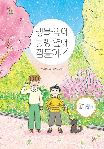 도서 『맹물 옆에 콩짱 옆에 깜돌이』의 표지. 벚꽃과 수많은 꽃들이 흐드러지게 핀 거리에 두 명의 아이가 나란히 서 있다. 왼쪽의 아이는 키가 크고 갈색 머리에 노란 티셔츠, 초록색 바지를 입었다. 오른쪽 아이는 작은 키에 진한 눈썹을 가지고 있으며 노란색 줄무늬 티셔츠에 검은색 바지를 입었다. 오른쪽 아이 곁에는 작은 검은 강아지가 앉아있고 오른쪽 아이는 한 손에 강아지 목줄을 쥐고 있다.