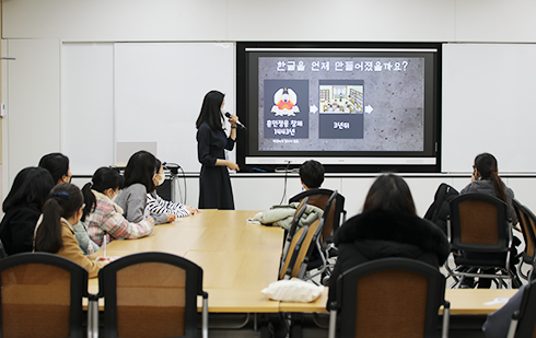 교육을 듣고 있는 학부모와 학생들이 화면을 보고 있다. 화면엔 ‘한글은 언제 만들어졌을까요?’에 대한 교육 내용이 쓰여 있고, 교육 담당자가 화면 옆에서 설명하고 있다.