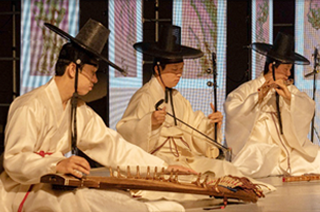 전통음악집단 샛의 공연 사진이다. 전통의상과 갓을 쓴 3명의 단원이 앉아서 제각각 전통 악기를 연주하고 있다. 