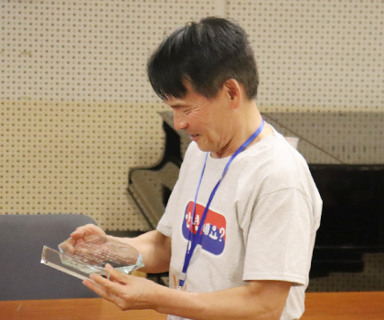 반갑습니다 사진. ‘안녕하세요?’가 적힌 흰색 반팔을 입고 있는 강병구 교수가 들고 있는 상패를 내려다보며 웃고 있다. 