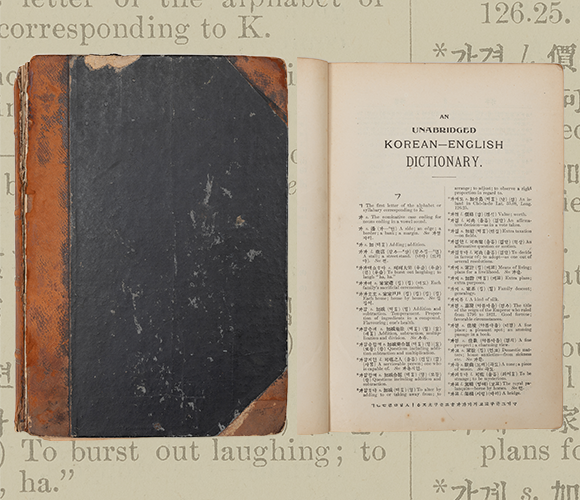 중앙에 외국인 선교사가 쓴 옛 한국어 사전 ‘한영자전’이 있다. 책은 검은색 표지이며, 오래되어 찢겨있고 낡은 느낌이다. 옆에는 한영자전의 ‘ㄱ’에 해당하는 페이지를 찍은 사진이 함께 놓여있다. 배경으로는 한영자전의 한 페이지를 확대한 사진이 흐릿하게 깔려있다.